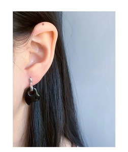 Close-up of minimalist black heart pendant earrings on a model with silver rings