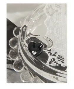 Detailed close-up of a silver heart ring with black enamel on a delicate lace background