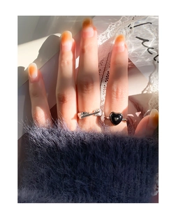 Detail of silver textured open ring and black enamel heart ring worn by a model