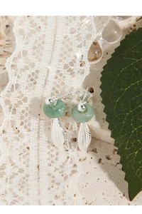 Macro shot of S925 sterling silver stamp and green jade feather earrings on marble