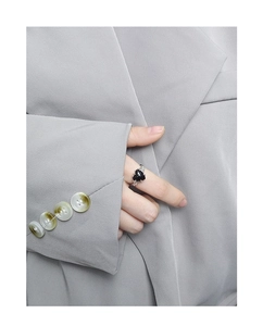 Gros plan d'une bague coeur en argent à texture irrégulière portée sur un blazer gris