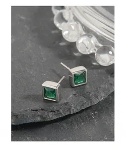 Detailed view of square emerald zircon stud earrings on dark grey natural rock surface