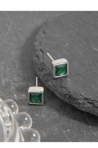 Macro detail of geometric S925 silver stud earrings with emerald green zircon gemstones