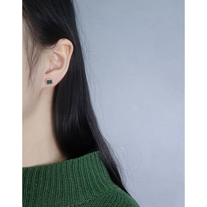 Close-up of minimalist S925 silver stud earring with emerald zircon on earlobe