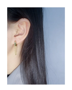 Détail de boucles d'oreilles pendantes à chaîne dorée portées par un mannequin au style épuré