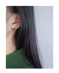 Close-up of shell-shaped silver earring worn by model against a white background
