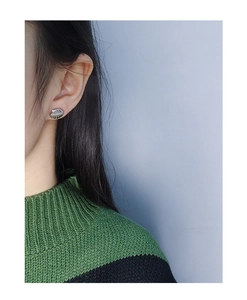 Detail view of shell-shaped S925 silver stud earring with vertical stripes on ear lobe