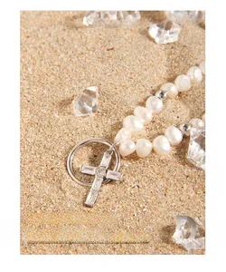 Détail d'un pendentif croix en argent S925 avec zircons et perles naturelles sur le sable