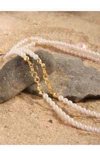 Detailed shot of pearl necklace with gold infinity clasp on natural stone and sand