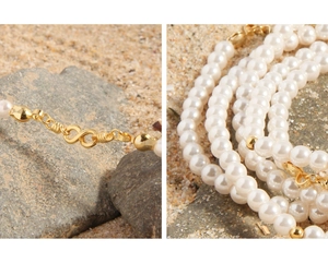 Macro shot of gold infinity clasp and lustrous white pearl layers on natural sand