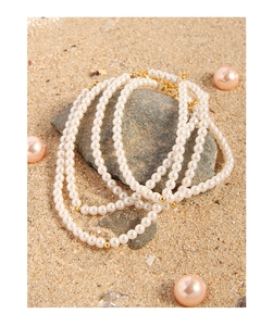 Detail of layered pearl necklace with gold clasp on beach stones, chic jewelry close-up