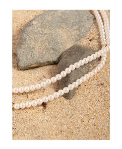 Close-up of minimalist white pearl necklace on natural sand and rock outdoor setting