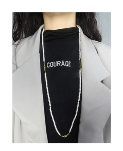 Detailed view of long white pearl necklace with gold accents worn over a black turtleneck
