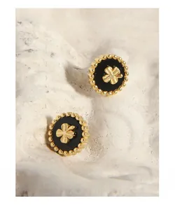 Macro detail of gold-plated clover earrings with black inlay on white stone surface