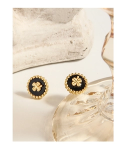 Detailed macro view of vintage gold clover stud earrings on relief glass with black enamel