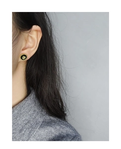 Close-up of a vintage black round stud earring with a golden four-leaf clover pattern