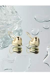 Macro detail of puffy gold heart earrings on a reflective surface with water droplets