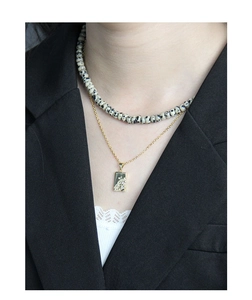 Detail of layered gold chain and spotted stone bead necklace on model in black suit