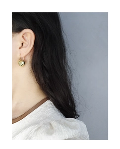Close-up of minimalist 3D heart earrings in polished gold on model ear