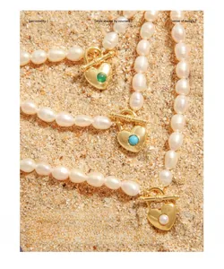 Detail of heart pendants with colorful beads on pearl necklaces over sand
