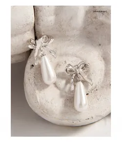 Close-up of S925 silver bow earrings with elegant white teardrop pearl pendants