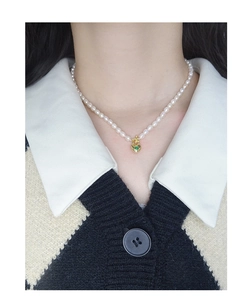 Detail of freshwater pearl necklace featuring a golden heart pendant with green gemstone