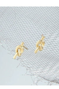 Detailed view of polished S925 sterling silver gold knot stud earrings on a metallic mesh