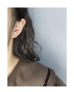 Detail of minimalist gold-tone knot stud earring worn by model in a stylish setup