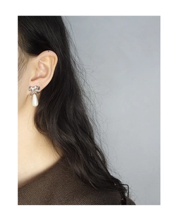 Detailed view of silver bow-knot stud earrings with teardrop pearls on ear