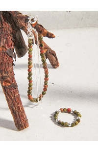 Détail de la bague et du bracelet en perles d'unskite sur support en bois naturel