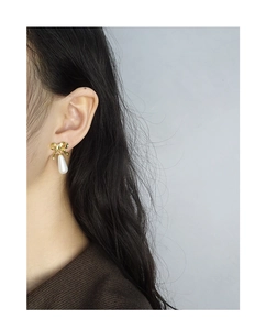 Detailed view of elegant gold bow earrings with white water drop pearls on a model