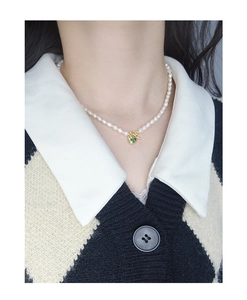 Close-up of pearl necklace with gold heart pendant and green gemstone on white shirt