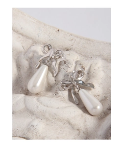 Detailed view of S925 silver bow stud earrings with white teardrop pearls on a stone base