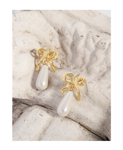 Detailed macro shot of golden bow earrings with teardrop pearls on a textured stone