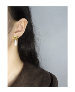 Detail view of elegant bow-knot gold earrings with teardrop pearl on female model