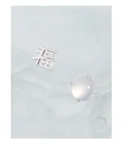 Macro view of asymmetric silver Fu character earrings and rounded white gemstone studs