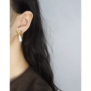 Elegant gold bow earrings with white teardrop pearl on female model in natural light