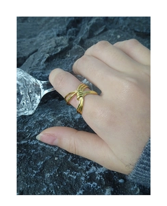 Dettaglio dell'anello multistrato dorato incrociato indossato su uno sfondo di roccia