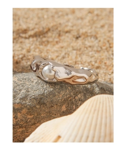 Detail eines S925 Silber-Perlenrings mit Lava-Struktur auf dunklem Felsen am Strand