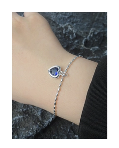 Detail of S925 silver bracelet with heart-shaped blue zircon on textured rock background