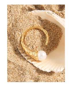 Macro detail of gold-plated wrinkled texture ring with a large white pearl in a seashell