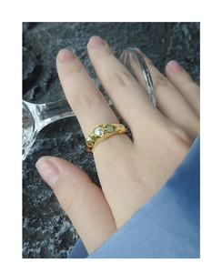 Nahaufnahme eines goldfarbenen Rings mit Faltenstruktur und weißer Perle am Finger