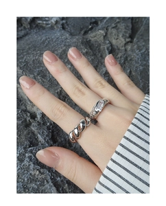 Detail of twisted silver chain ring and rectangular stone set on a grey rock background