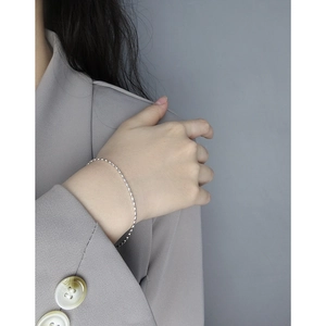 Bracelet minimaliste en argent sterling S925 porté par un mannequin en veste grise