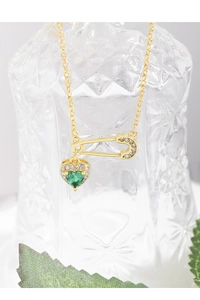 Macro detail of gold safety pin pendant with emerald green heart stone and zircon pave