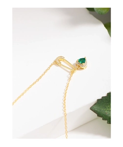 Macro view of gold safety pin necklace with green emerald heart pendant and crystals