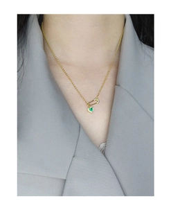 Close-up of a golden safety pin necklace featuring a green heart pendant on a model
