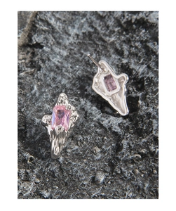 Macro detail of irregular silver earrings with pink zircon on volcanic rock texture