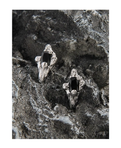 Macro detail of irregular S925 silver stud earrings with black zircon on volcanic rock