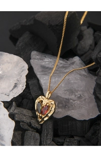 Detail of gold heart pendant with textured ripples and inlaid teardrop gemstones